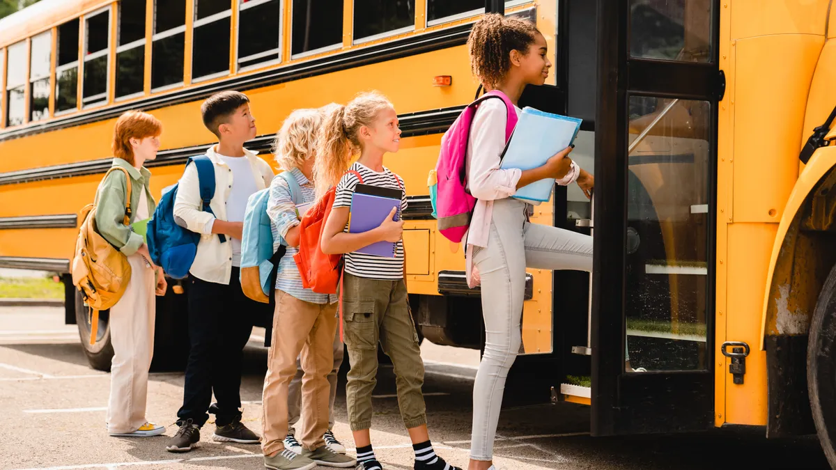 Schoolchildren kids pupils group of mixed-race classmates boarding school bus before going to lessons