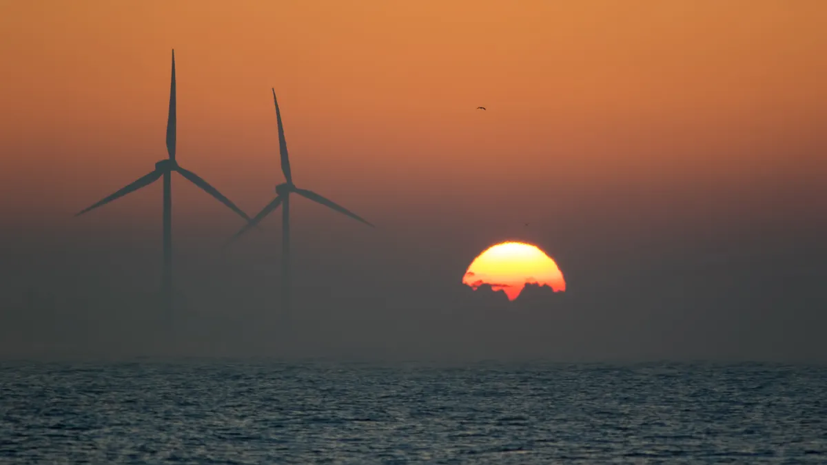 Two offshore wind turbines on the sea with a sunrise on the horizon.