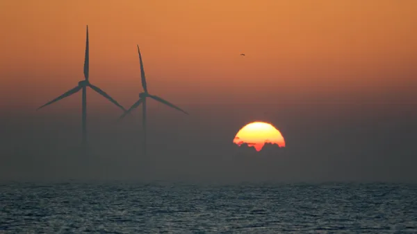 Two offshore wind turbines on the sea with a sunrise on the horizon.