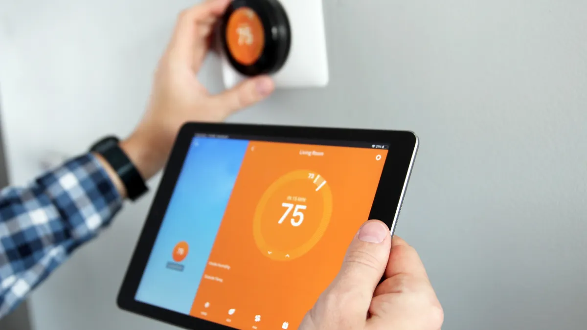 Man is adjusting a thermostat using a tablet with smart home app in modern living room.