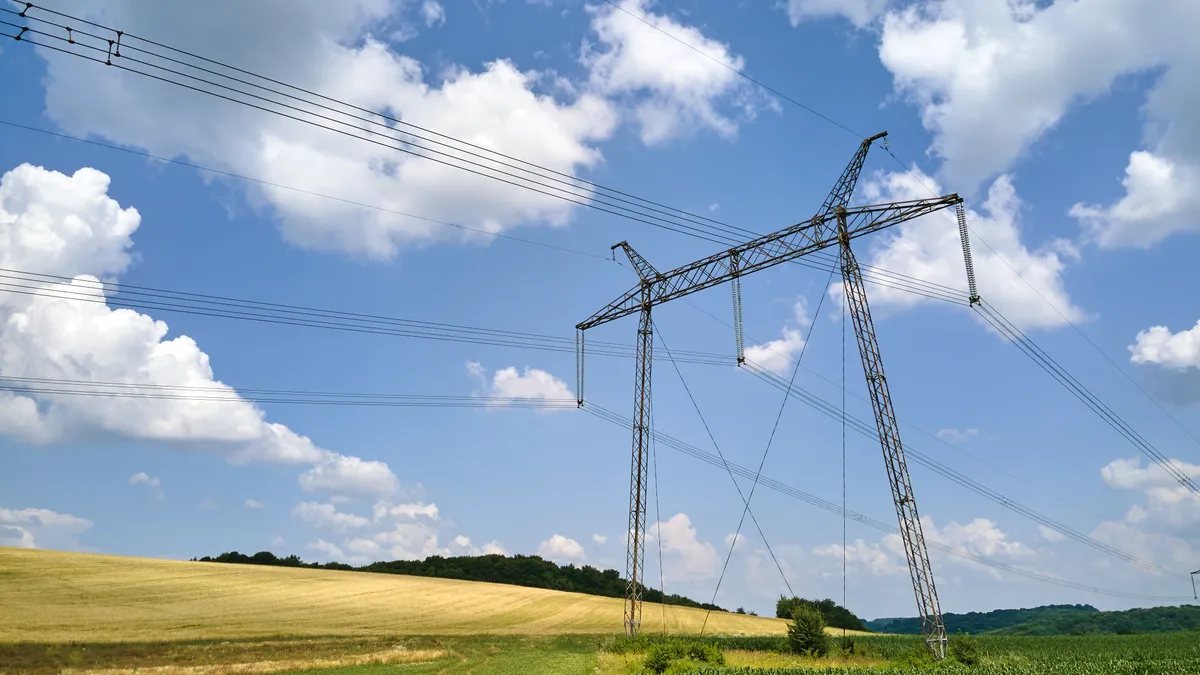 Pylons carrying electric wires over an agricultural field with blue sky and fluffy, white clouds in the background.